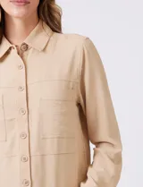 Camisa de crepe color beige con cuello clásico, cierre frontal con botones y dos bolsillos aplicados en el pecho.