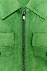 Chaqueta corta de tejido efecto ante en color verde vibrante, con cuello solapa, cierre frontal de cremallera y mangas largas. Presenta dos bolsillos frontales con solapa decorados con arandelas metálicas en el pecho.