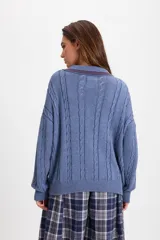 Sweater de punto trenzado color azul, con cuello polo, cierre frontal de tres botones y detalle de etiqueta roja en el puño.