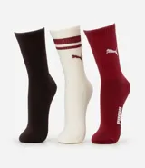 Kit de tres pares de medias deportivas Puma de caña larga. Un par es beige con dos rayas marrones y logo de Puma. Otro par es blanco liso. El tercer par es marrón oscuro con dos rayas blancas y logo de Puma. Todas están confeccionadas en algodón.