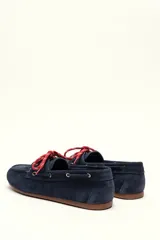 Mocasín tipo boat shoe color marrón, confeccionado en cuero, con cordones de cuero marrón y cordones decorativos azules.