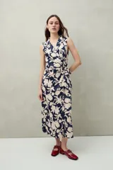 Vestido midi sin mangas con cruce delantero tipo wrap y lazo en la cintura. Presenta cuello sastrero y un estampado floral grande en azul marino y beige claro.