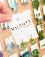 Aros colgantes con aro dorado y dije de flor verde agua con detalles en blanco. El aro mide 1,5cm de diámetro y la flor 1,5cm de diámetro. El aro es de acero y la flor de acrílico.