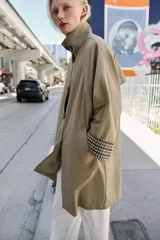 Trench de corte oversize color beige, con cuello alto, cierre frontal de botones y mangas largas con puños vueltos estampados a cuadros. Cuenta con bolsillos delanteros de vivo.
