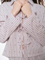 Camisa de dormir de popelina de algodón, con estampado de rayas verticales y pequeños motivos geométricos. Presenta cuello camisero, mangas largas y cierre frontal mediante lazos ajustables.