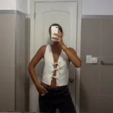 Chaleco blanco sin mangas, con escote en V profundo y cierre frontal mediante lazos anudados.