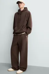 Pantalón jogger de corte relajado y pernera ancha, confeccionado en tejido de algodón con interior perchado. Presenta cintura elástica con cordón interior, bolsillos laterales y un bolsillo trasero de plastrón.