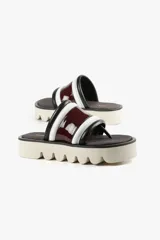 Sandalia con base alta y diseño de líneas audaces. Presenta capellada ancha con acabado brillante y estructura acolchada que aporta confort al andar. La suela dentada le da un carácter urbano y moderno, sin resignar comodidad.