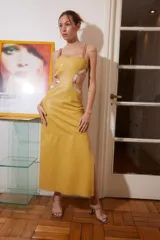 Vestido midi de cuero color maíz con cortes laterales y detalles dorados. Tiene tiras finas fucsias y abertura lateral en la falda.