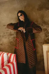 Campera larga acolchada color marrón, con diseño matelassé, detalles de piel sintética en el cuello y puños, y bordados artesanales en crochet color rojo en los bolsillos y costuras.