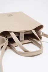 Bolso shopper mediano de nylon color beige con estructura blanda, doble asa corta de mano y correa fina ajustable. Cuenta con cierre de botón a presión, bolsillo interior con cierre y aplique metálico con el logo de la marca en el frente.