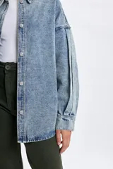Sobrecamisa de jean en tono celeste con efecto lavado, corte oversize, cuello clásico, cierre frontal con botones metálicos y mangas largas con detalle de frunces en los hombros.