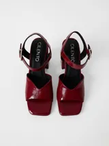 Sandalia de cuero charolado color bordó, con diseño de punta cuadrada, taco cuadrado forrado y tira ajustable al tobillo con hebilla metálica.