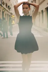 Vestido corto negro sin mangas, con cuello redondo y diseño de falda con volumen tipo globo. Presenta un corte entallado en el torso y cierre de cremallera oculta en la espalda.