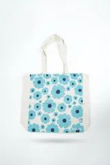 Bolso tipo tote bag de color crudo con estampado de flores celestes y centros azul oscuro. Cuenta con doble asa de hombro en tono crudo y etiqueta con la marca en el frente.