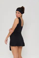 Vestido corto deportivo negro, sin mangas, con cuello redondo y detalle de lazo anudado en la cintura. Presenta el logo 'bk.' estampado en blanco en el pecho.