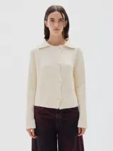 Cardigan de punto acanalado color crema, con cuello polo, cierre frontal de botones tejidos y manga larga.