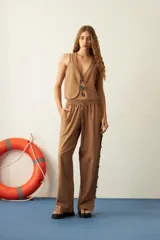 Pantalón marrón de corte recto, con cintura elastizada y cordón ajustable. Presenta mostacillas decorativas en los laterales.