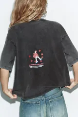 Camiseta de corte oversize con efecto lavado, cuello redondo y manga corta. Presenta una estampa gráfica central que representa una figura femenina sobre un pastel decorado con cerezas.