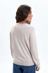 Saco de punto básico color beige, con cuello redondo, manga larga y cierre frontal con botones dorados.