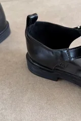 Sandalias tipo guillermina color negro, con diseño de tiras entrelazadas, talón cerrado, suela plana y tira ajustable con hebilla metálica en el lateral.