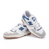Championes urbanos New Balance modelo 550, con diseño retro inspirado en el básquet de los años 80. Presentan una combinación de cuero sintético blanco, detalles en azul y gris, y suela de caucho color caramelo.