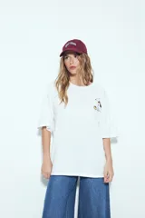 Remera blanca de manga corta, cuello redondo y calce relajado. Presenta un pequeño estampado frontal de un perro con un hueso y un estampado grande en la espalda con la frase "WILD HEART" y un diseño gráfico.