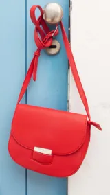 Bandolera de cuero sintético en color rosado, con diseño de solapa redondeada y cierre metálico frontal. Cuenta con correa ajustable para llevar al hombro o cruzada.