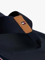 Ojotas de hombre color azul marino con tiras textiles trenzadas y apliques de cuero sintético marrón con el logo de Tommy Hilfiger. La suela presenta capas en azul marino, blanco y rojo.