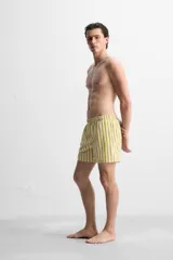 Short de baño confeccionado en tejido técnico, con diseño de rayas verticales amarillas y verdes sobre fondo blanco. Cuenta con cintura elástica ajustable con cordón, bolsillos laterales y bolsillo trasero con vivo.
