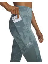 Calza deportiva Under Armour de tiro alto, confeccionada en tejido HeatGear de secado rápido con estampado camuflado en tonos azulados. Presenta paneles laterales lisos con perforaciones láser para mayor transpirabilidad, bolsillo lateral y detalles reflectantes en la parte inferior de la pierna.