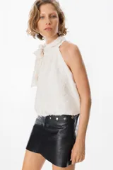Blusa blanca sin mangas con cuello halter y lazo lateral. Confeccionada en tela de gasa con textura floreada en relieve.