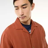 Camisa de manga corta confeccionada en tejido de punto fantasía de algodón, en tono marrón terracota. Cuenta con cuello solapa, abotonadura frontal y corte recto.
