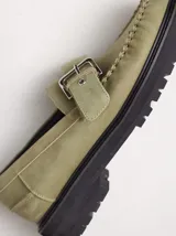 Mocasines de cuero color verde militar con suela track negra y capellada cosida. Cuenta con una tira con hebilla metálica ajustable en el empeine.