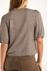 Blusa de algodón con estampado de cuadros vichy en tonos negro y blanco. Presenta escote en V, cierre frontal con botones y mangas cortas abullonadas con terminación elástica.