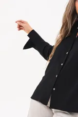 Camisa de manga larga color negro, de cuello redondo con frunces, abotonada en el frente y puños abiertos con tajo.
