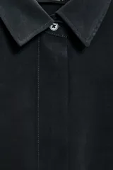 Camisa de corte fluido con cuello solapa y manga corta con dobladillo. Presenta cierre frontal con botones ocultos bajo una tapeta.