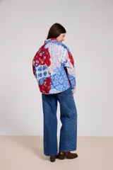 Campera de estilo camisa con diseño capitoneado y estampado patchwork que combina motivos florales, paisley y cuadros en tonos rojos y azules. Presenta cuello camisero, cierre frontal con botones y bolsillos delanteros.