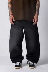 Jean de denim negro con lavado oscuro, corte extremadamente ancho y holgado (baggy), tiro medio-alto y largo que arrastra sobre el calzado.