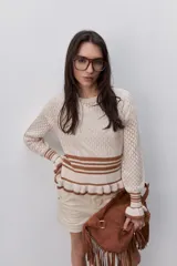 Sweater de tejido calado color beige, con cuello redondo, mangas largas y detalles acanalados a rayas en contraste en los puños y en el ruedo con volados.