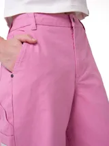 Pantalón de carpintero marca Cat, color rosado, de corte relajado, con bolsillos utilitarios, presilla para martillo y cierre frontal con botón y cremallera.