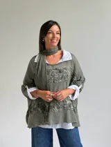 Sweater de punto color verde oliva con diseño de paneles horizontales de encaje floral, corte holgado y mangas tres cuartos. Incluye una bufanda del mismo tono y tejido, y se presenta superpuesto sobre una camisa blanca de cuello clásico.