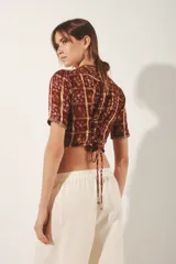 Saco corto estilo crop top con cuello redondo y mangas cortas. Confeccionado en tejido jacquard con lurex, presenta un estampado en tonos borgoña y dorado, y está ricamente bordado a mano con hilos y espejos (mostacillas). Cierre frontal con ganchos ocultos.