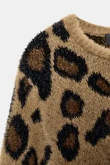 Chaqueta de punto con textura suave, cuello redondo y manga larga. Presenta un diseño de estampado animal print en tonos marrones y negros, con cierre frontal de botones.