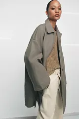 Trench oversize de Zara Woman Collection, confeccionado en hilatura de algodón. Presenta cuello solapa, manga larga, bolsillos delanteros y cierre frontal con botones ocultos bajo solapa.