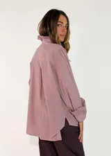 Camisa de algodón color blanco, con cuello redondo y detalle de volados en el cuello y puños. Presenta mangas largas con puños elásticos y un diseño de corte holgado con ruedo asimétrico, más largo en la parte trasera.