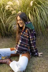 Buzo tipo canguro de corte oversize, confeccionado en paño de lana con diseño de rayas horizontales en tonos marrón, blanco y azul. Presenta una capucha amplia y un cuello de piel sintética en color verde oscuro.