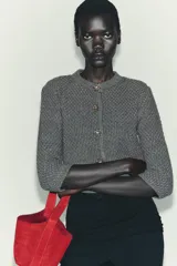 Chaqueta de punto grueso color gris, de cuello redondo y manga tres cuartos. Cierre frontal con botones joya dorados con detalles de pedrería. Cuenta con dos bolsillos frontales tipo parche.