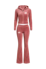 Conjunto de dos piezas confeccionado en terciopelo rosa, compuesto por un buzo con capucha y cierre frontal, y un pantalón de corte acampanado. Ambas prendas presentan un estampado gráfico circular con el número 27.