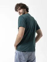 Remera Merrell de manga corta en color verde oscuro, cuello redondo y diseño estampado en el pecho con gráfico de montañas y logotipo de la marca.